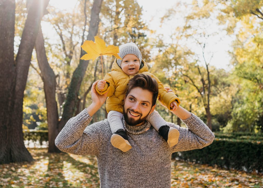 Father carrying his son on his shoulders outdoors in autumn