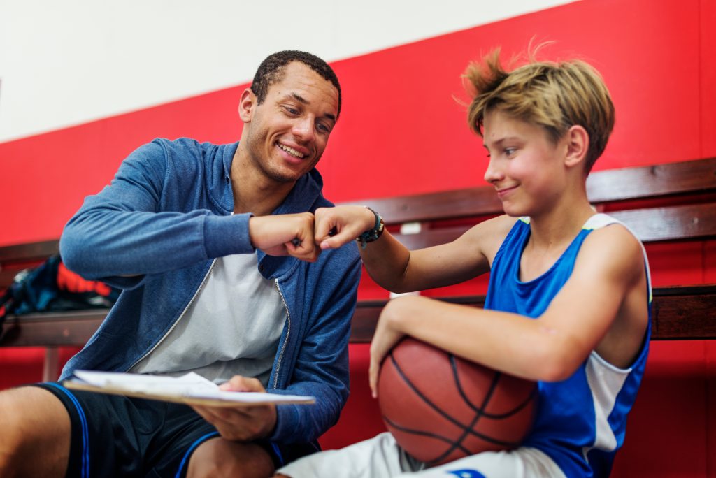 Coach fist-bumping a young basketball player holding a ball